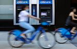 Cyclists wearing protective masks ride past a Citibank branch.