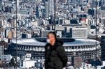 This picture taken on January 19, 2021 shows the National Stadium (back), the main venue for the Tokyo 2020 Olympic and Paralympic Games, as a visitor (front) stands at the Shibuya Sky observation deck in Tokyo. - When the Tokyo Olympics were postponed last year, officials promised they would open in 2021 as proof of humankind's triumph over the coronavirus. But six months before the delayed start, victory over the virus remains distant, and fears are growing rapidly that the Games of the 32nd Olympiad may not happen at all. (Photo by Philip FONG / AFP) / TO GO WITH AFP STORY OLY-2020-2021-JAPAN-VIRUS-HEALTH BY ANDREW MCKIRDY (Photo by PHILIP FONG/AFP via Getty Images)
