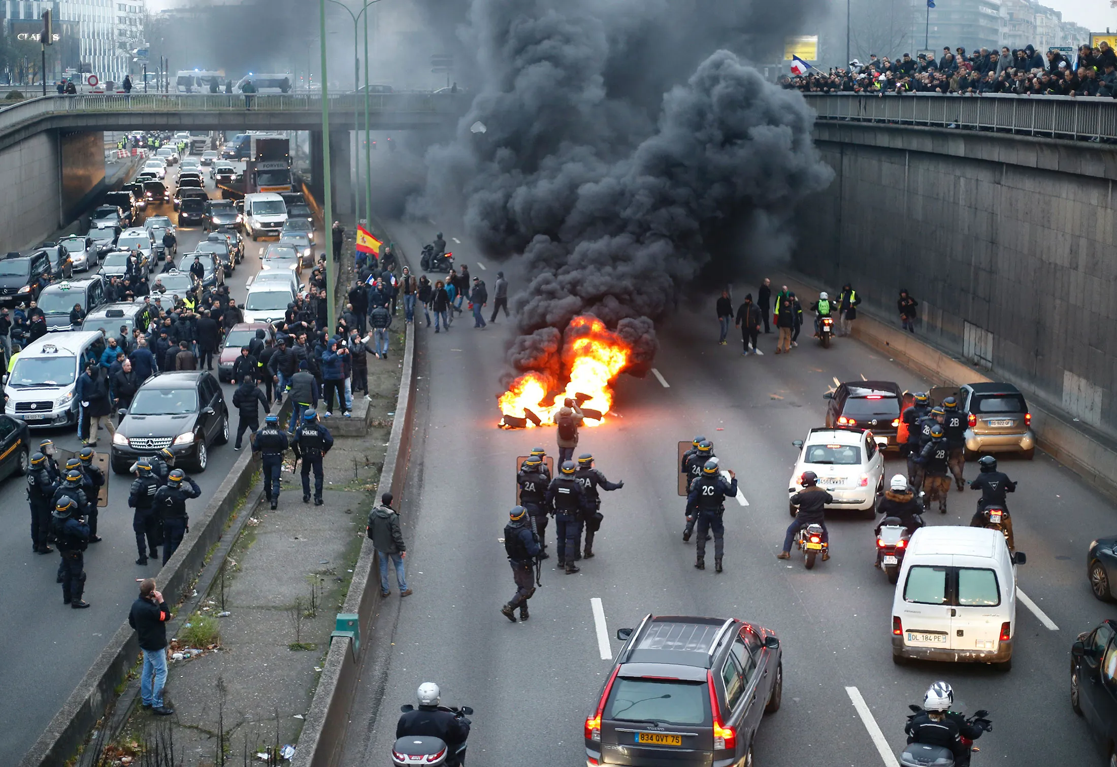 Anti-riot policemen arrive as taxi drivers block the traffic with a fire during a demonstration against the VTC (transport vehicle with chauffeur) on Jan. 26, 2016 at porte Maillot in Paris.
