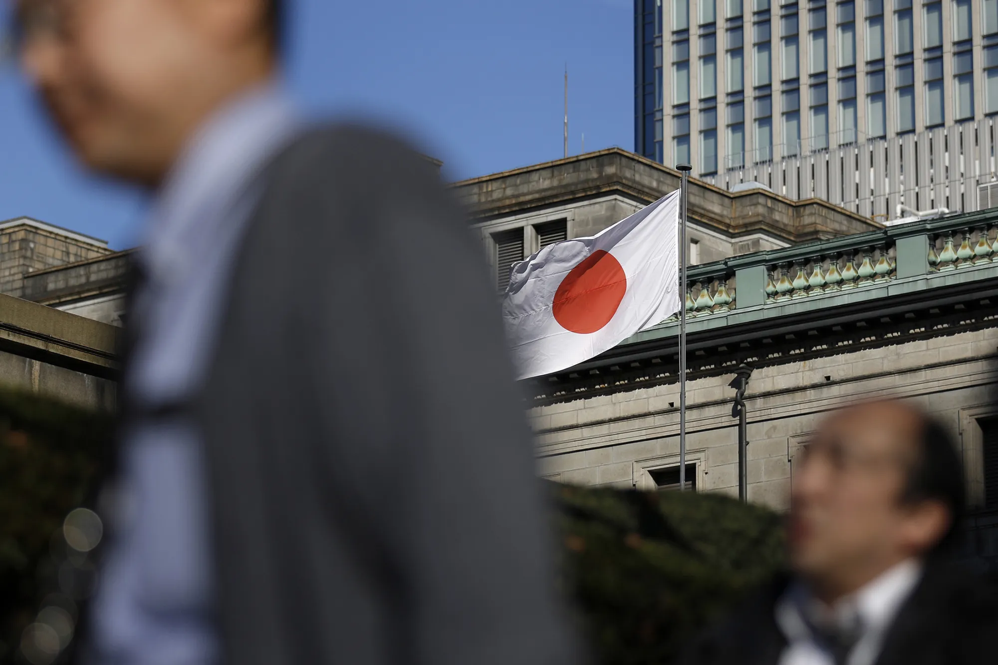 The Japanese national flag flies outside the Bank of Japan headquarters in Tokyo, Japan, on Friday, Dec. 19, 2014. The Bank of Japan maintained unprecedented stimulus, as Governor Haruhiko Kuroda's bid to stoke inflation faces increasing challenges from the tumble in oil prices.
