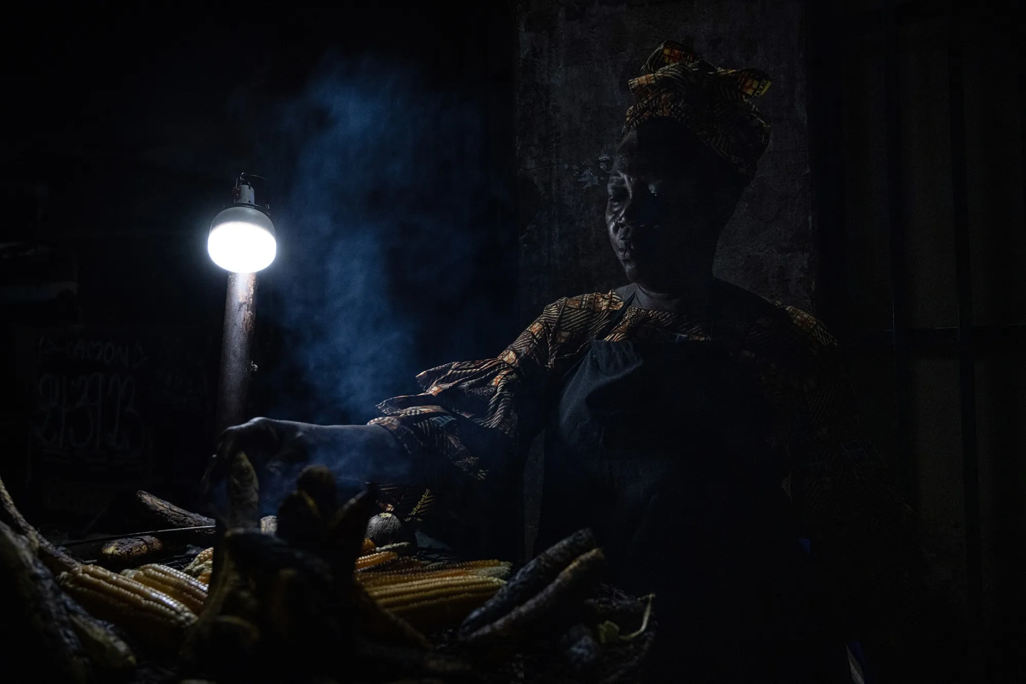 A street vendor in Lagos, Nigeria, roasts corn and plantains at night under a bright rechargeable bulb during a power outage.