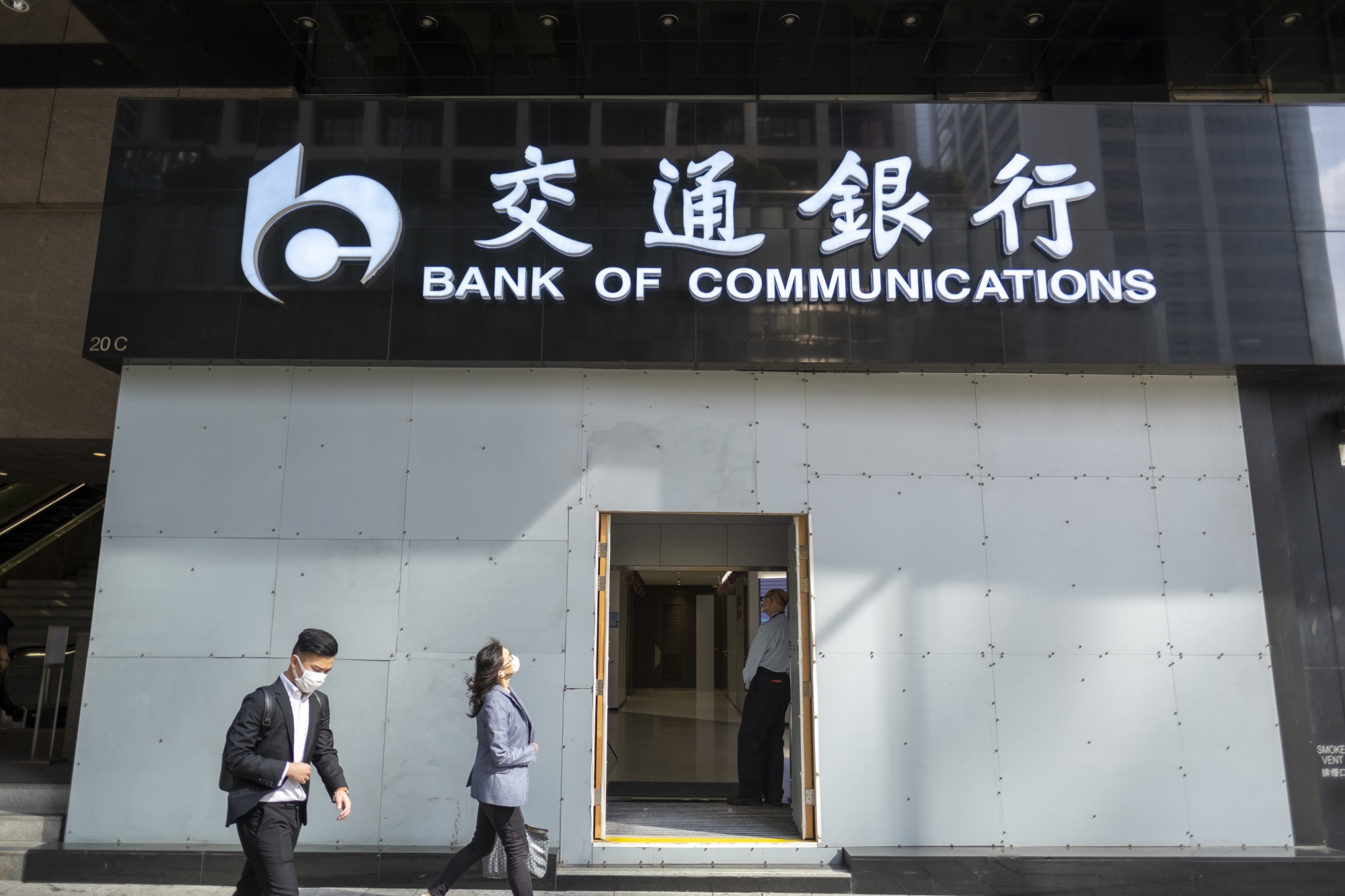 Pedestrians walk past a Bank of Communications Co. branch in Hong Kong.