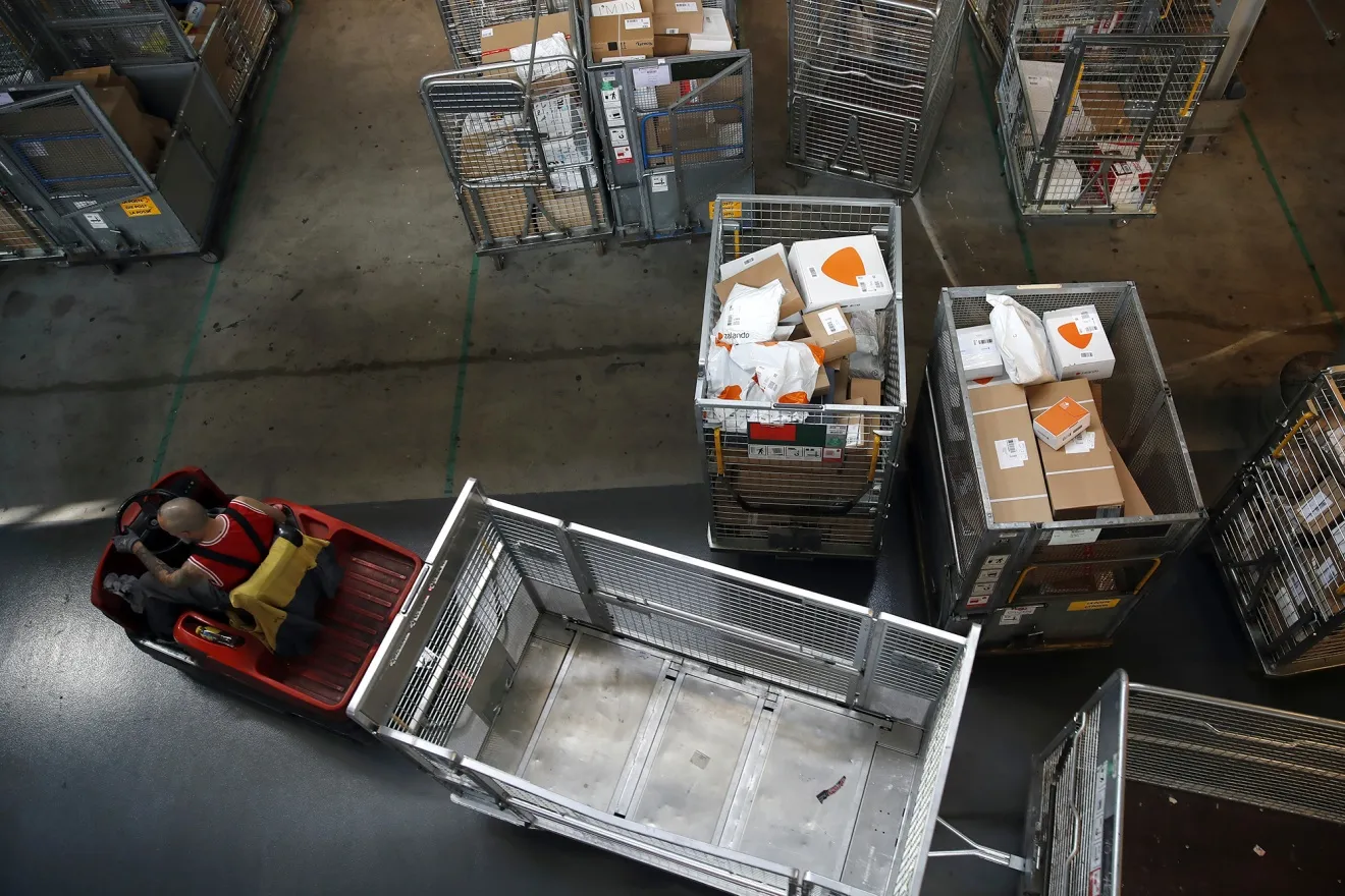 An employee drives a cart pulling empty parcel trolleys at a Swiss Post&nbsp;parcel sorting center in Harkingen, Switzerland.