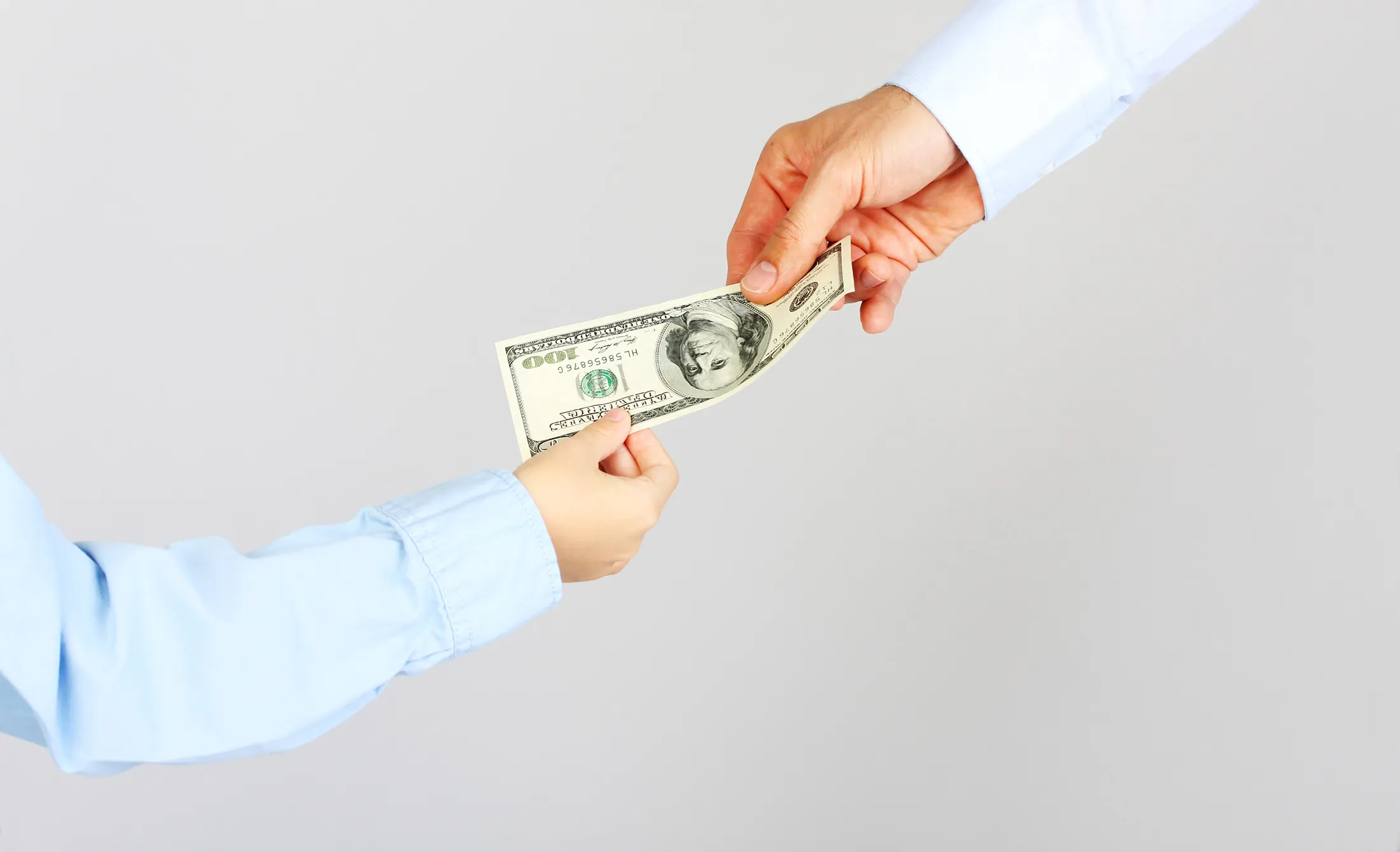 Man's hand give money american hundred dollar bills to boy hand. Business man give money business boy. Father and son.
