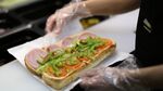 An employee prepares a sandwich inside a Subway restaurant.
