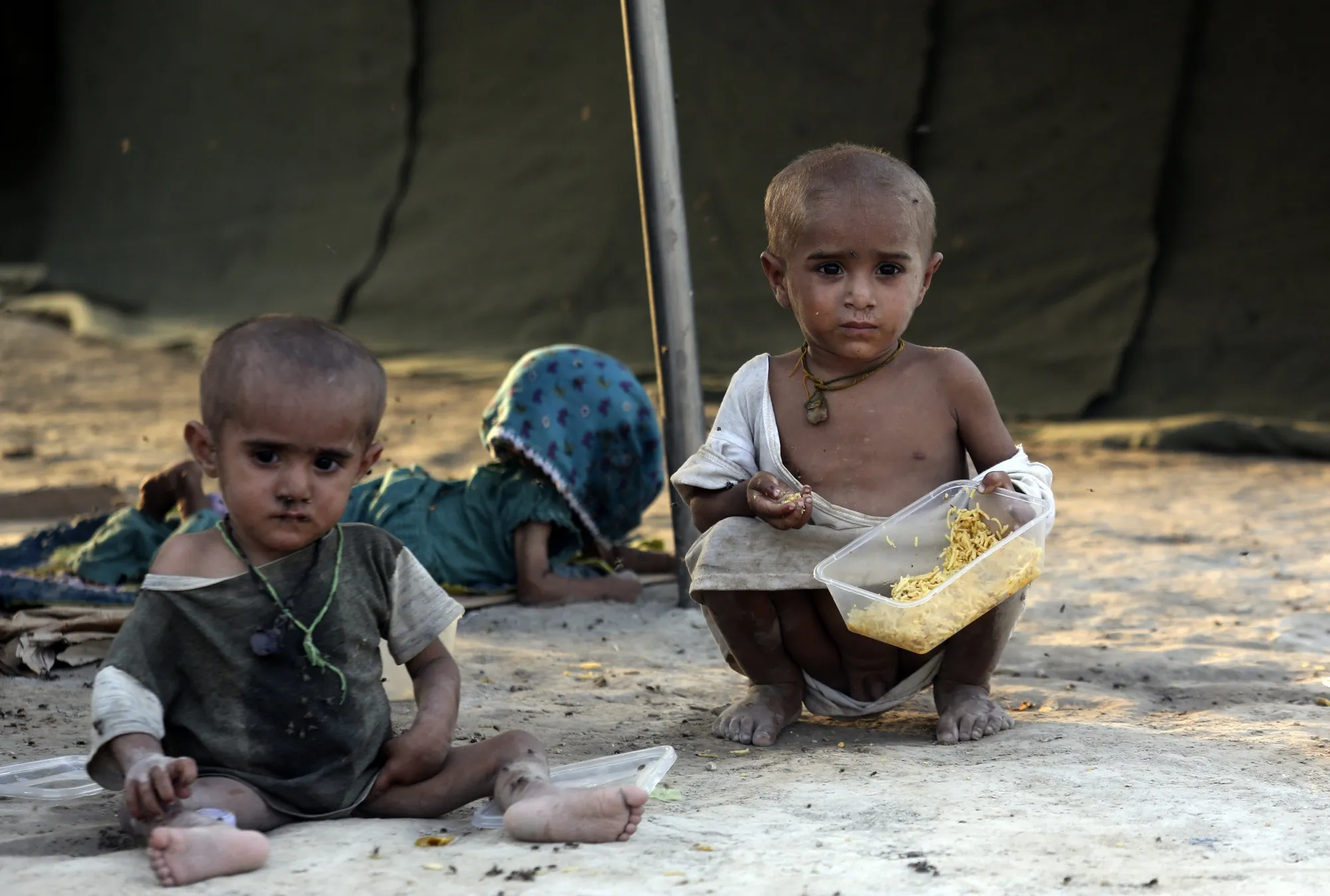 Children displaced by flooding from monsoon rains eat food at a temporary tent housing camp  for flood victims and organized by the China government, in Sukkur, Pakistan, Wednesday, Sept. 7, 2022. (AP Photo/Fareed Khan)