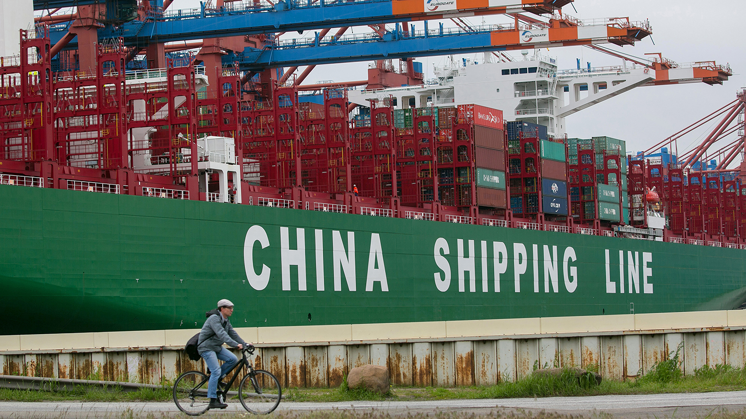 A man cycles past the CSCK Indian Ocean container ship, operated by China Shipping Container Lines Co., during loading operations at the Eurogate GmbH &amp; Co. KGaA KG shipping terminal at Hamburg port in Hamburg, Germany, on Tuesday, June 2, 2015.
