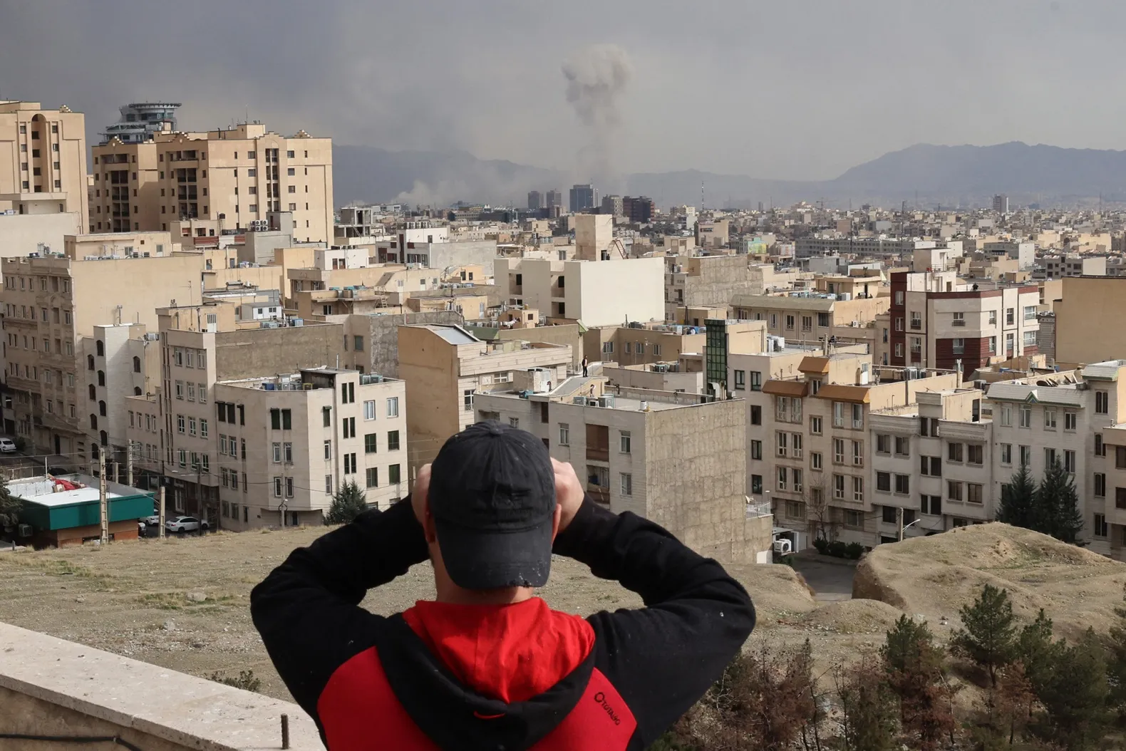 A man looks through binoculars as a plume of smoke rises after a military strike in Tehran on March 2.