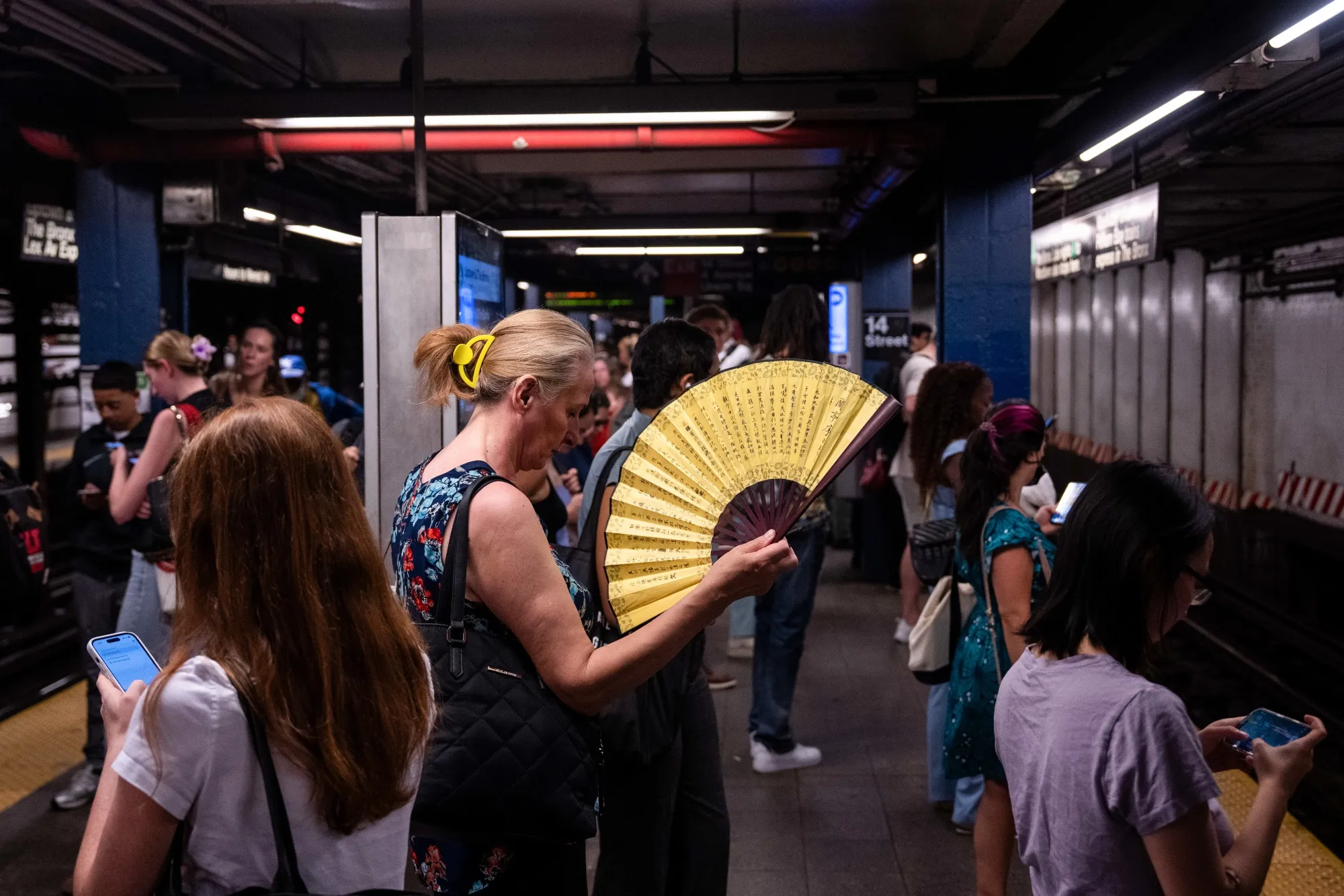 A commuter uses a handheld fan in a subway station during high temperatures in New York in June.