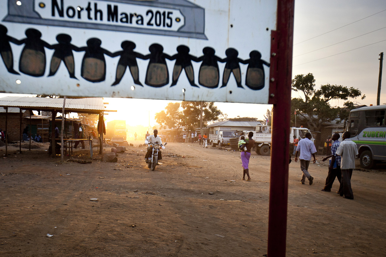 A motorcycle and pedestrians pass along a dirt road in the district of Nyangoto, Tanzania.