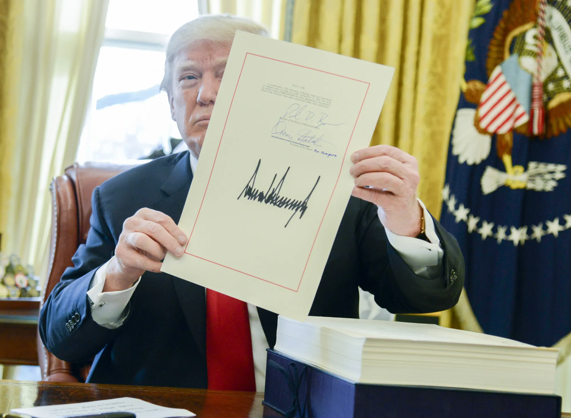 U.S. President Donald Trump holds up the&nbsp;tax-overhaul bill after singing it into law.
