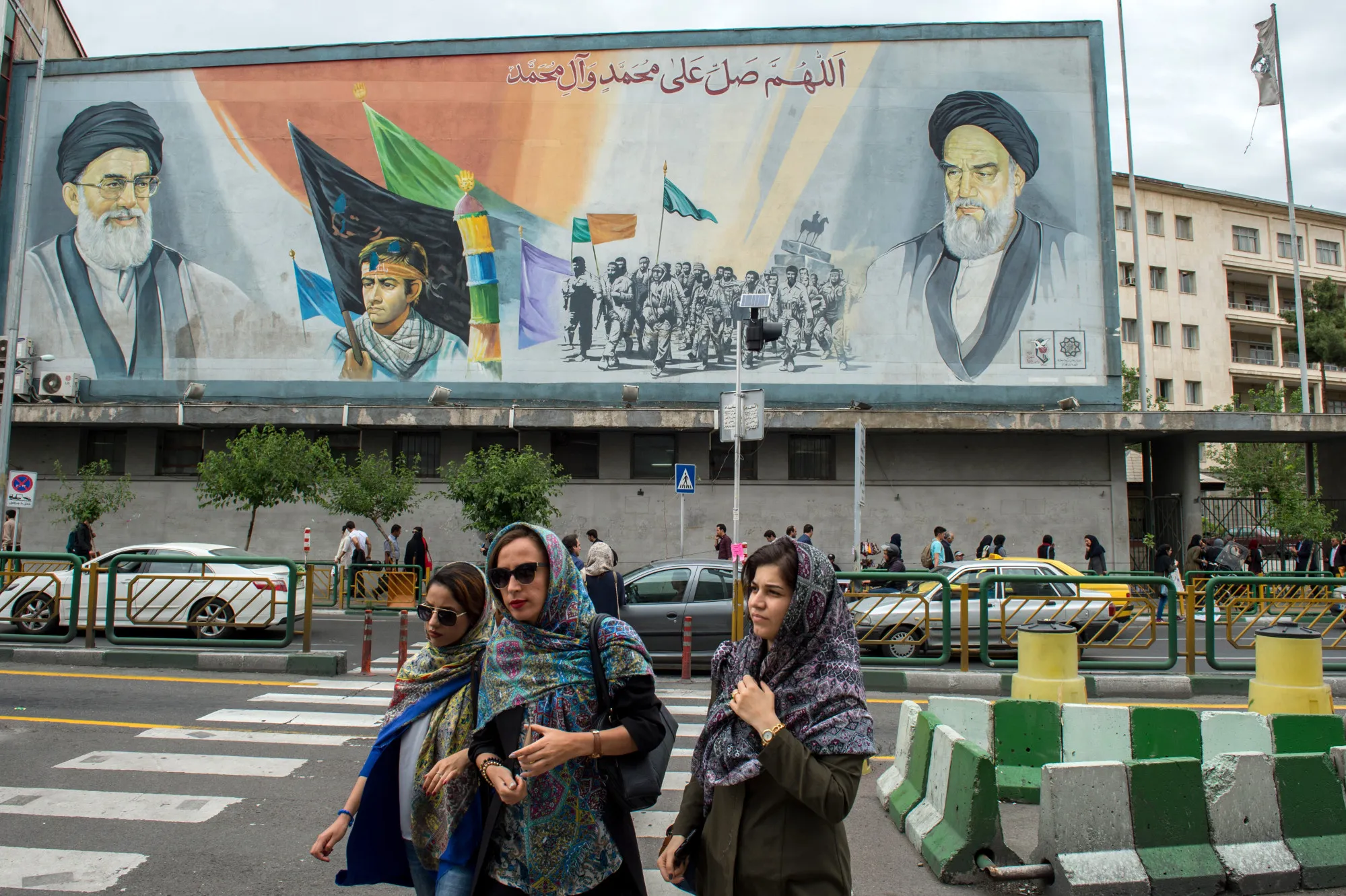 Women cross a street near a giant political mural depicting Ayatollah Ali Khamenei, Iran's supreme leader, left, and Ruhollah Khomeini, founder of the Islamic republic of Iran, in Tehran.