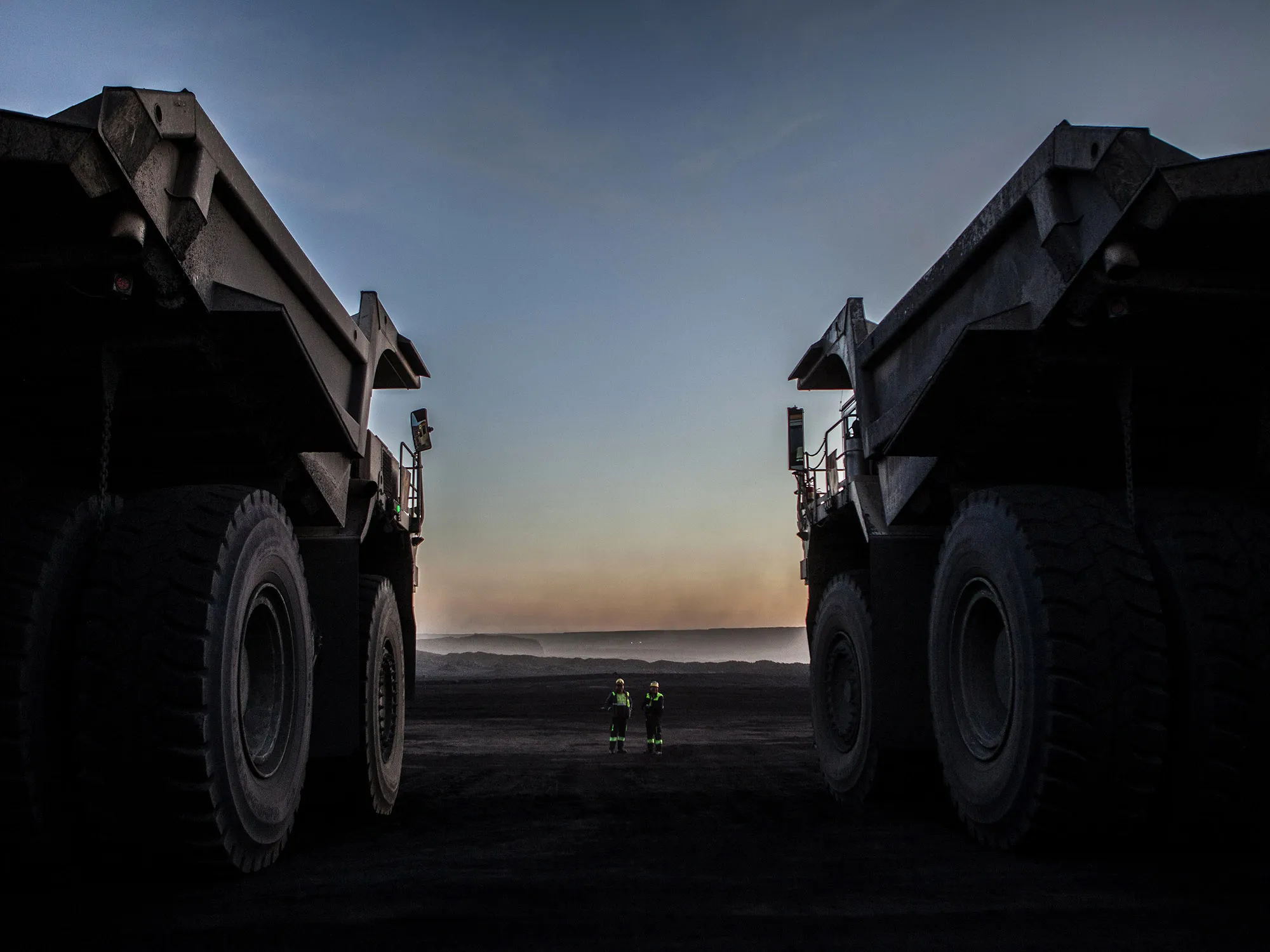 Workers stand near dump trucks at a mine.