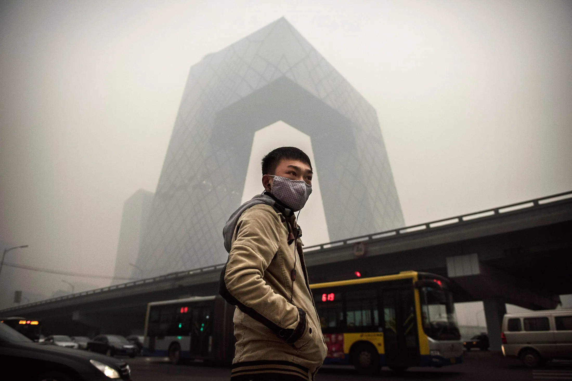 A man wears a mask as he waits to cross a road near the CCTV building during heavy smog on Nov. 29, 2014, in Beijing.
