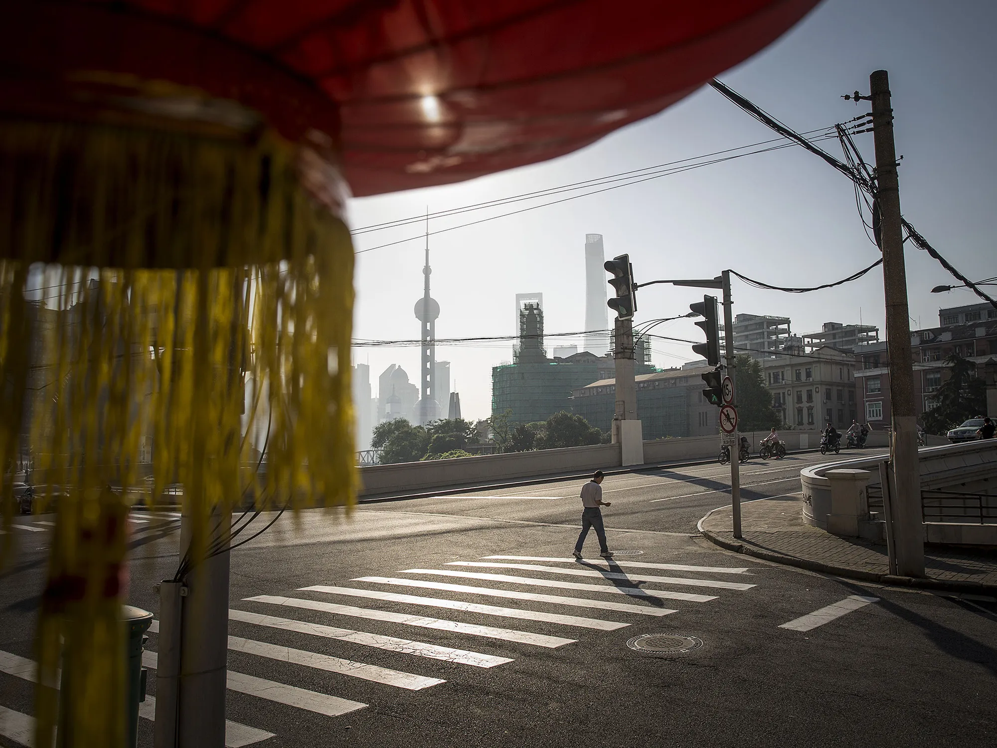 A pedestrian crosses a road as buildings of Pudong's Lujiazui financial district.