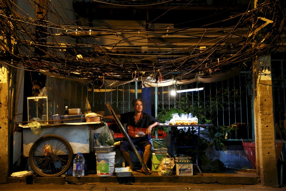 A man sells food under a canopy of wires in Bangkok.