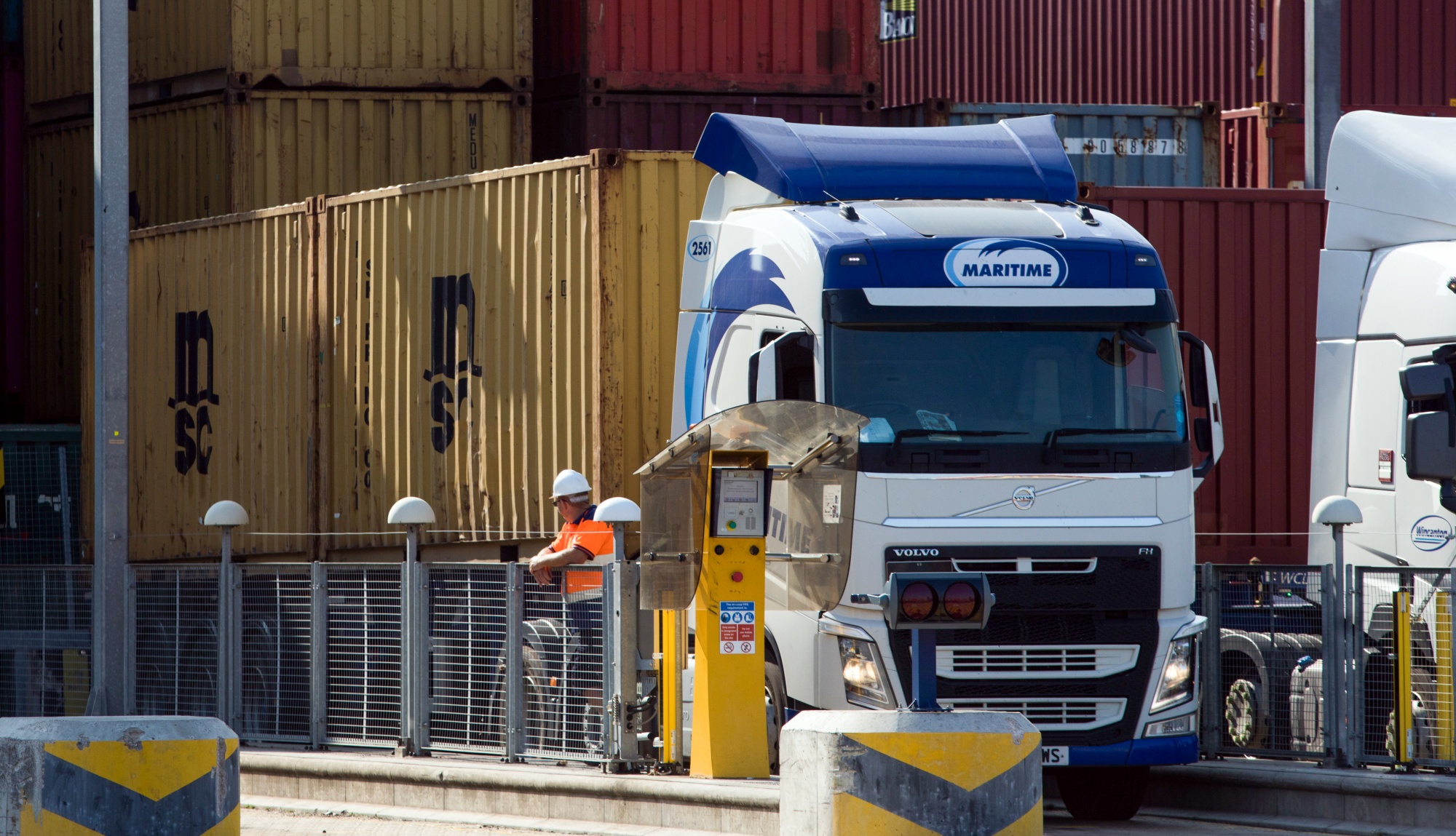 An employee stands next to a truck carrying a shipping container on the dockside at London Gateway port,in Stanford-le-Hope, U.K.