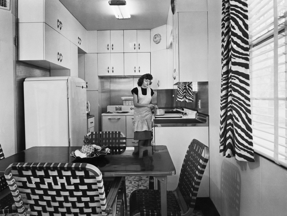 A woman cooks in a small 1940s-era kitchen.