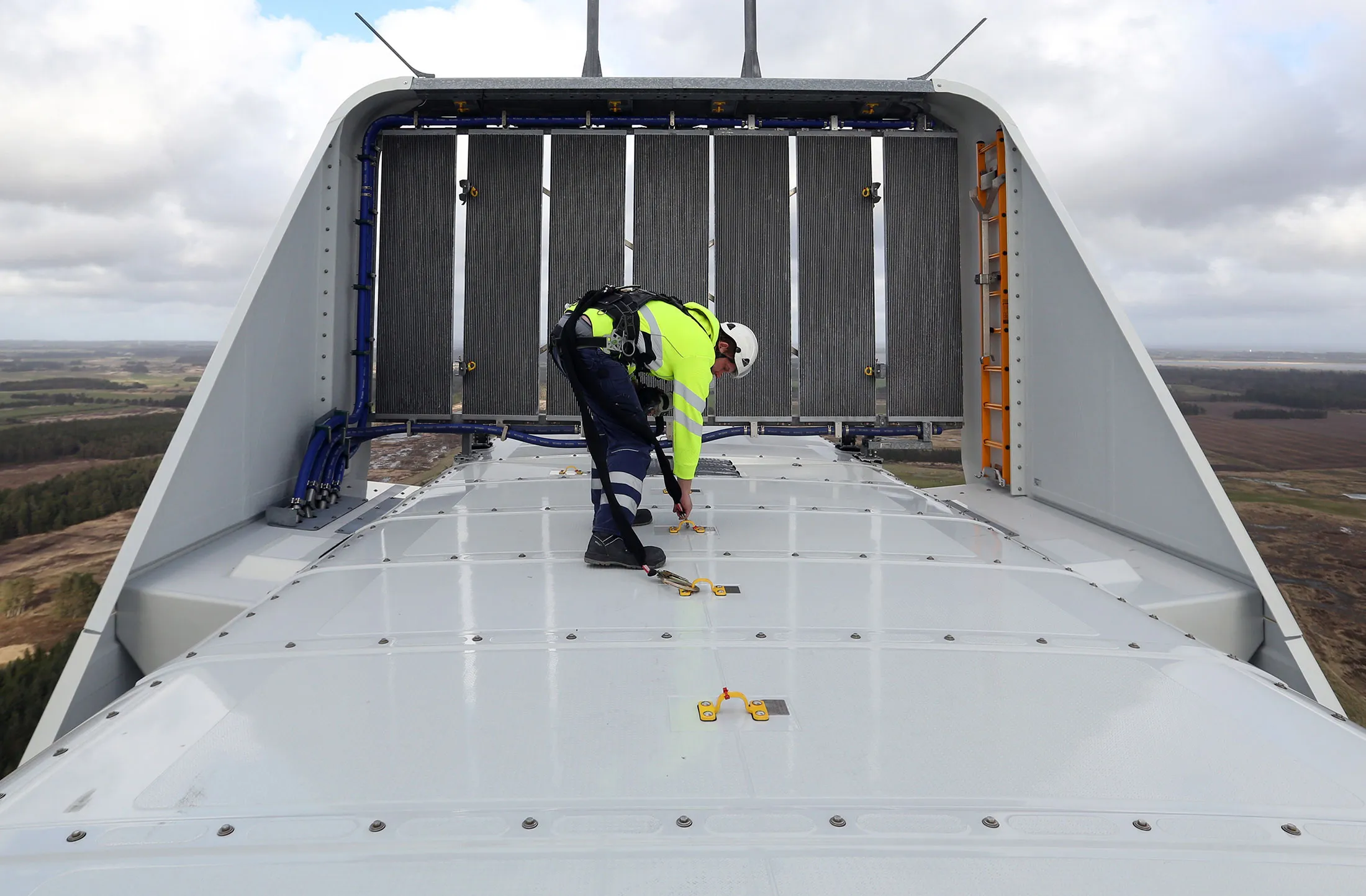 An employee clips a safety harness to an anchor point on the nacelle of a Vestas A/S V136 wind turbine.

