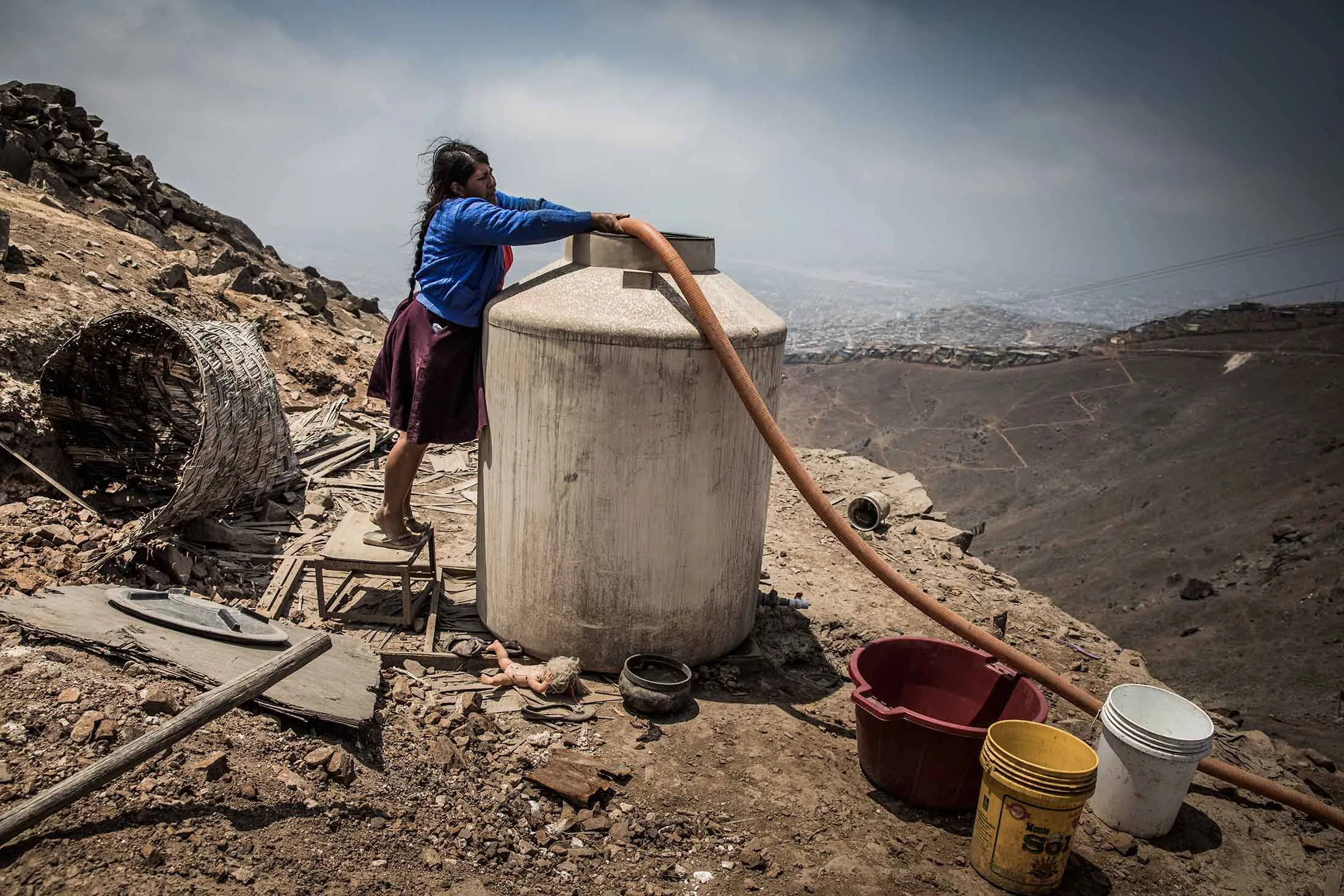Rosa Gonzales Aliaga uses a hose connected to a water supply truck to fill her tank in San Juan de Miraflores, an outer district of Lima, Peru.
