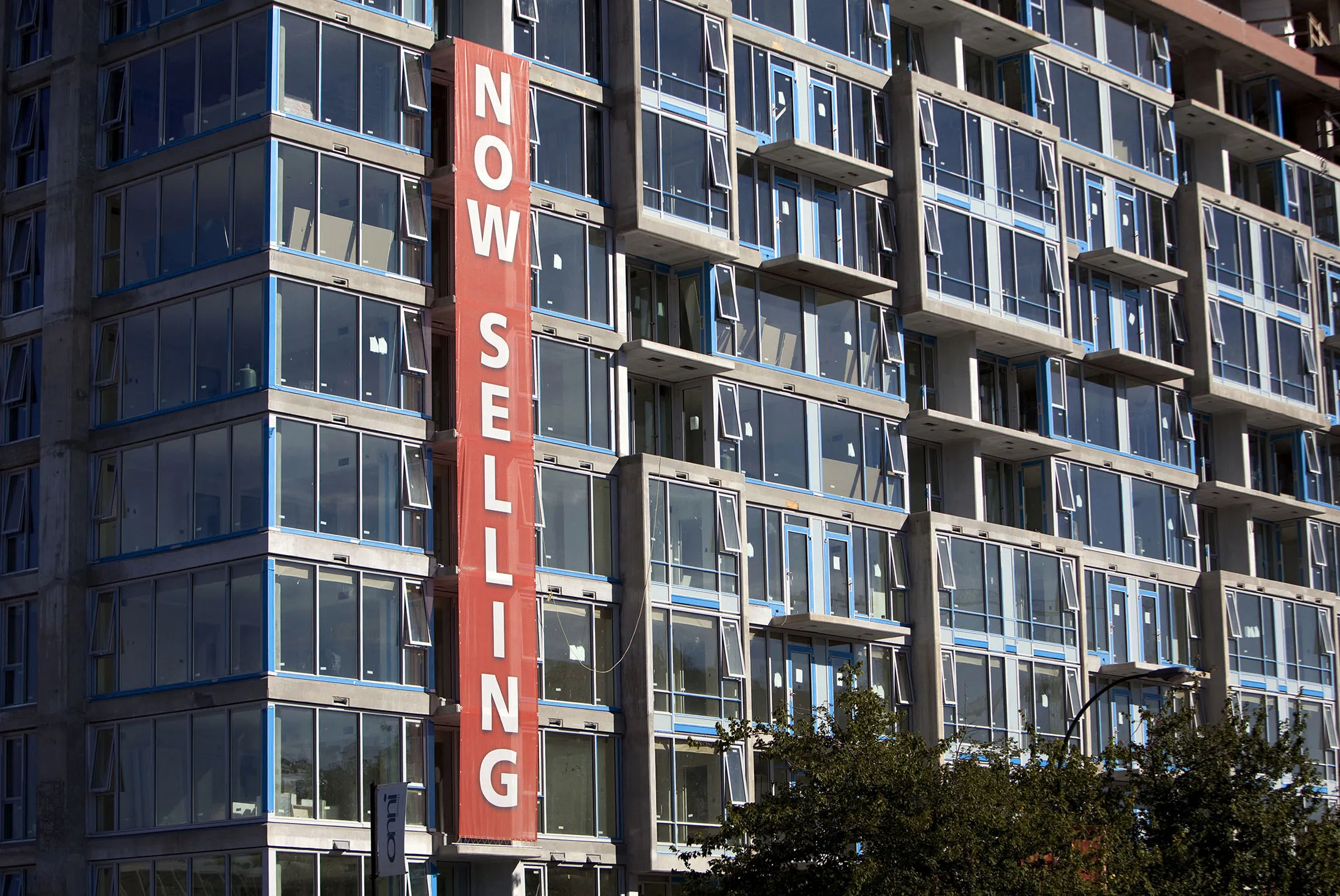 A "Now Selling" sign is displayed at a condominium under construction in Vancouver.
