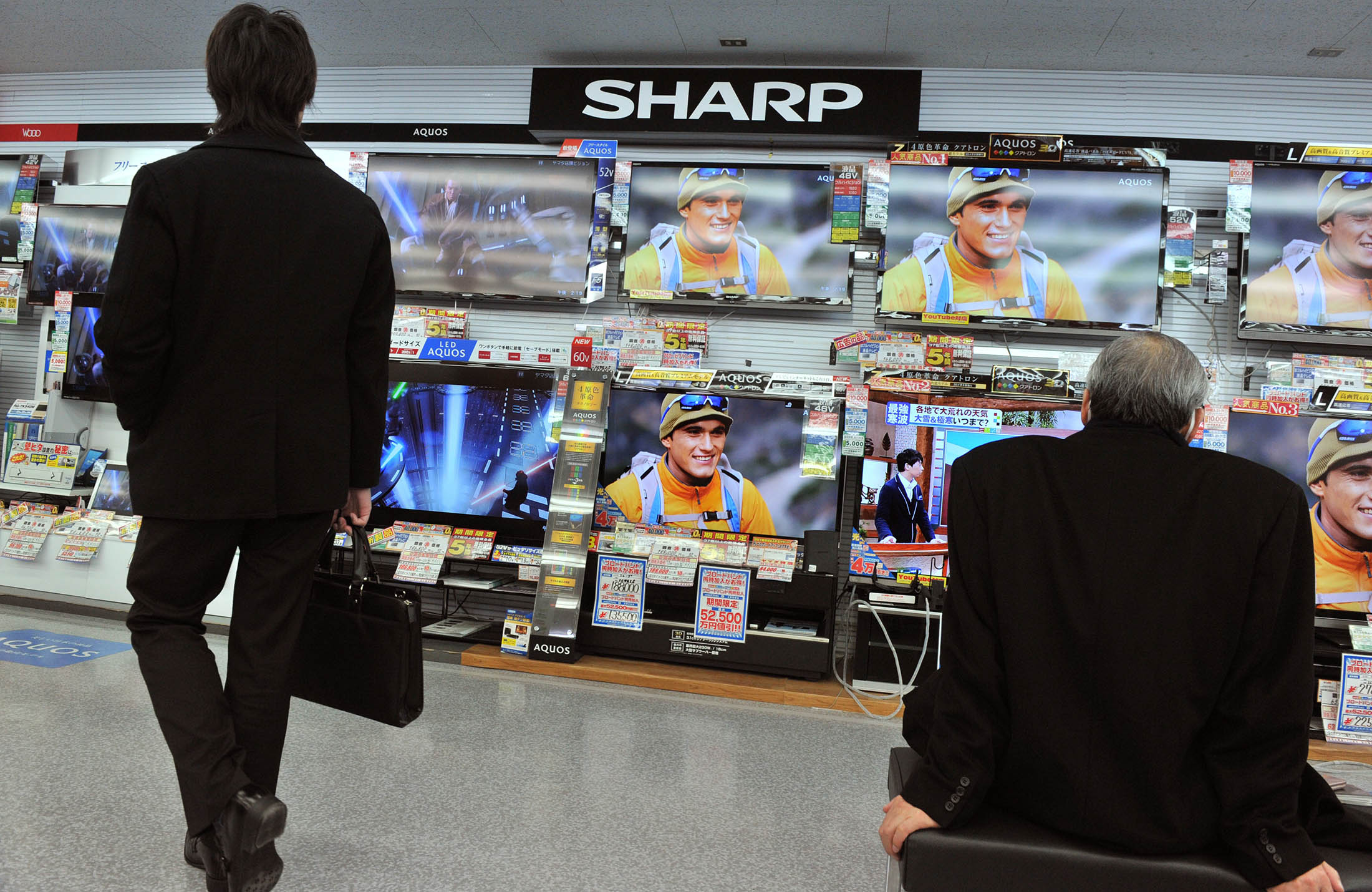 (FILES) This file photo taken on February 1, 2012 shows customers watching televisions under a Sharp logo at an electrical shop in Tokyo. Shares in Japan's Sharp dived almost 30 percent to their lowest level in nearly four decades on August 3, 2012, after the consumer electronics giant warned its annual loss would be bigger than first thought. AFP PHOTO / FILES / KAZUHIRO NOGI (Photo credit should read KAZUHIRO NOGI/AFP/GettyImages)
