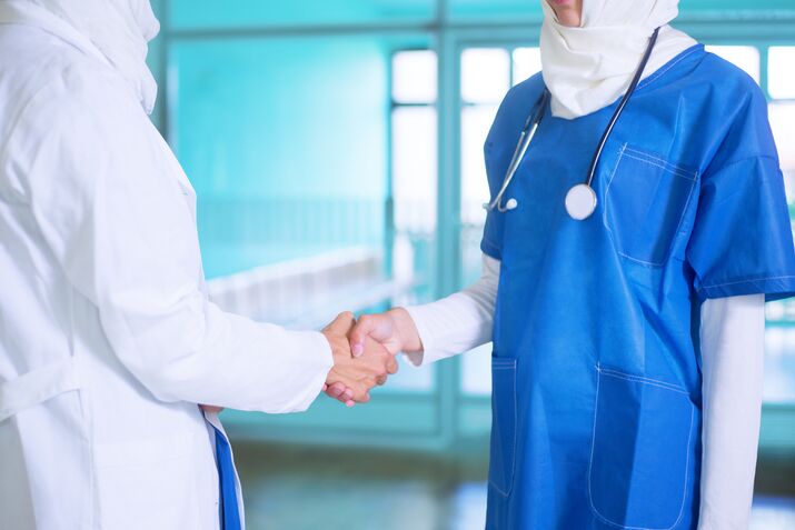 Close-up photo of young female arabic doctor and a nurse  white and blue medical uniform and a white hijab shaking hands