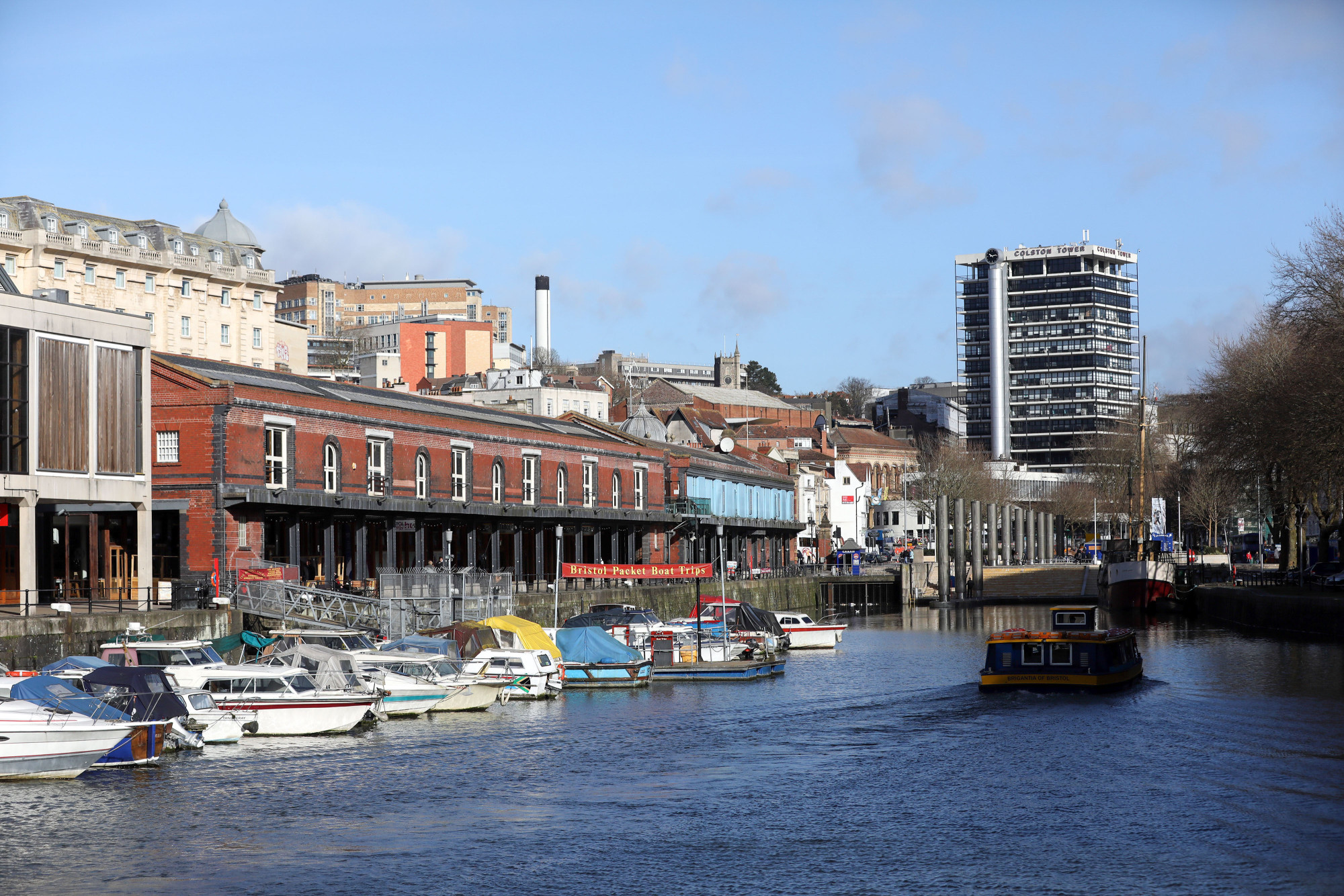 Boats sit moored on the harborside as a river ferry passes by in Bristol, U.K.
