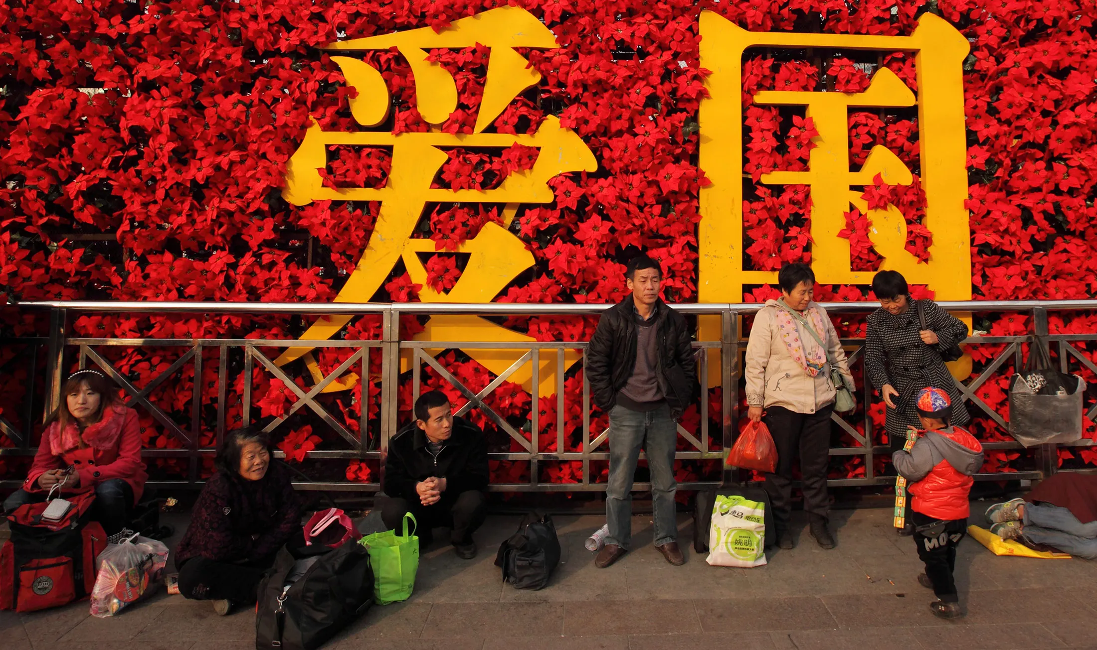 People are seen resting in front of a floral flower display which reads 'patriotism' in Chinese characters in Beijing.
