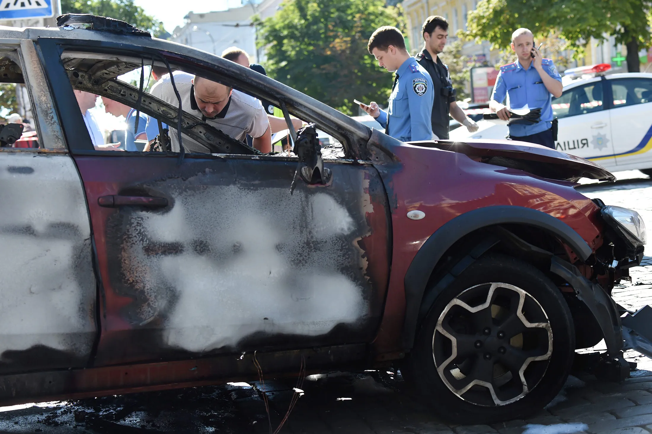 Ukrainian police officers and security services experts examine the charred car of journalist Pavel Sheremet, after he was killed in a car bomb in Kiev on July 20, 2016.
