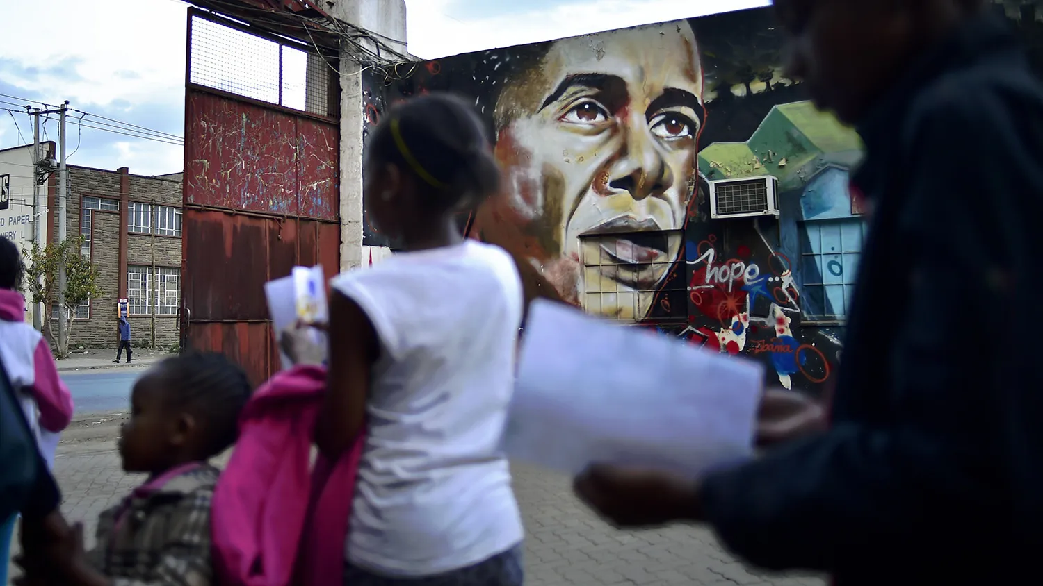 People walk past a graffiti representing US President Barack Obama is seen on a wall in Nairobi on July 25, 2015. Kenyans gathered in the city centre to watch US President Barack Obama's convoy as it drove through Nairobi. Obama is on a 5 day East Africa state visit. In addition to visiting Kenya, he will also visit Ethiopia. Obama's father, Barack Obama Senior was born in Kenya in 1936. President Obama has visited Kenya in the past most recently in 2006. Obama has a large following amongst Kenyans because of his familiy lineage. AFP PHOTO / CARL DE SOUZA (Photo credit should read CARL DE SOUZA/AFP/Getty Images)
