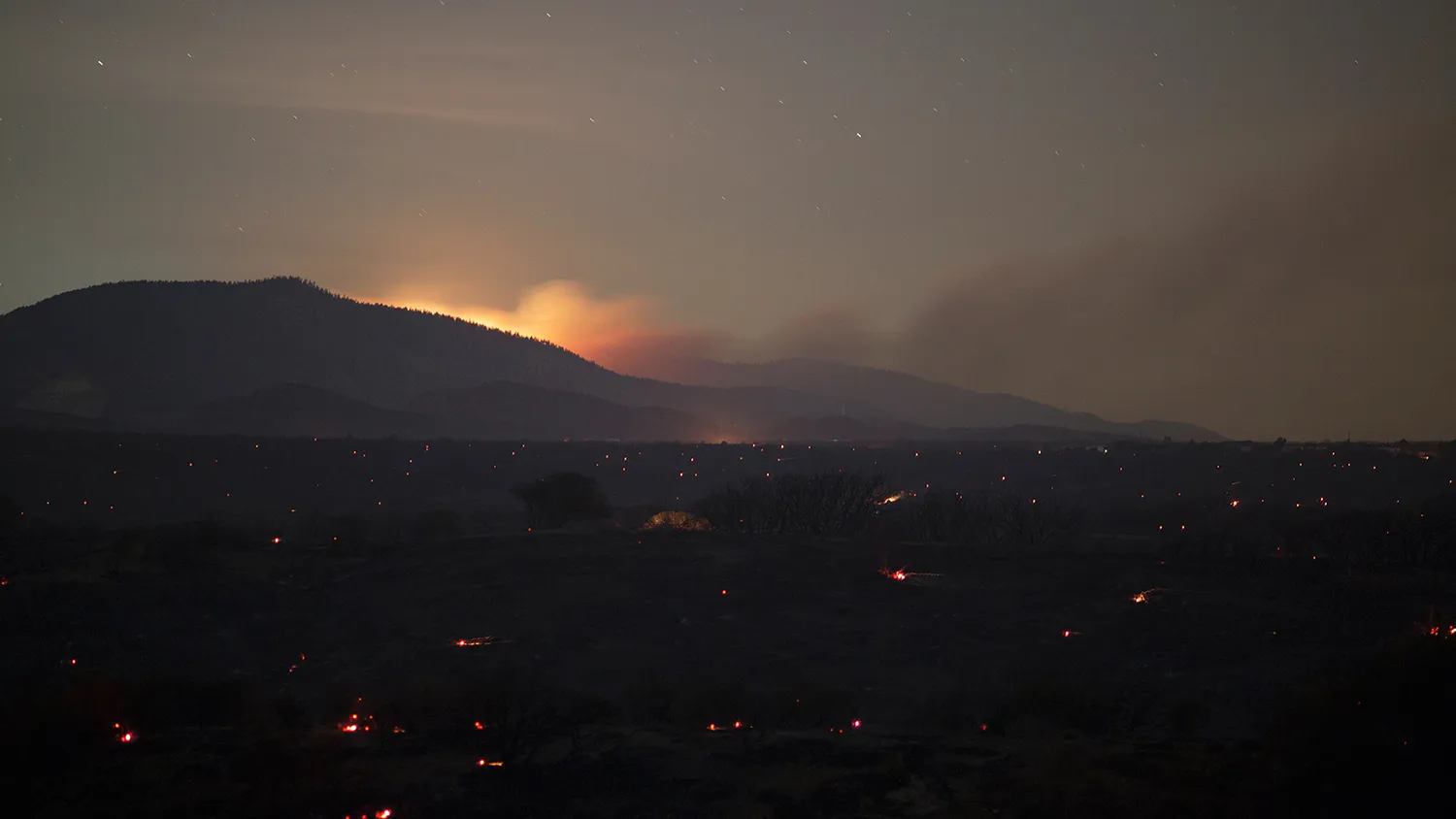 A new fire, being dubbed the Pine Fire, is seen in the distance as a landscape of embers burns in the wake of the North Fire, which caused people to abandon their vehicles and flee as flames jumped the 215 freeway in the early morning hours of July 18, 2015 near Victorville, California.
