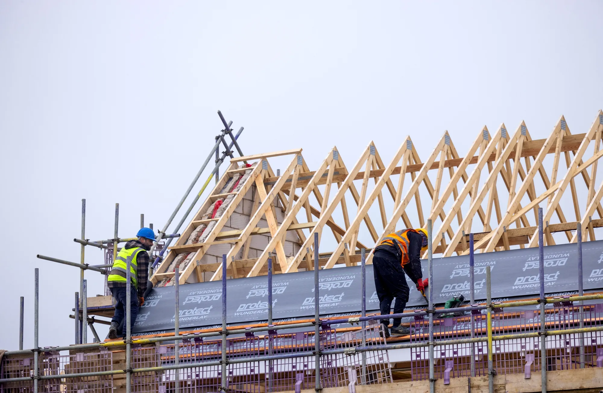Employees lay roof insulation material on joists at a Persimmon Plc residential property construction site in Braintree, UK.