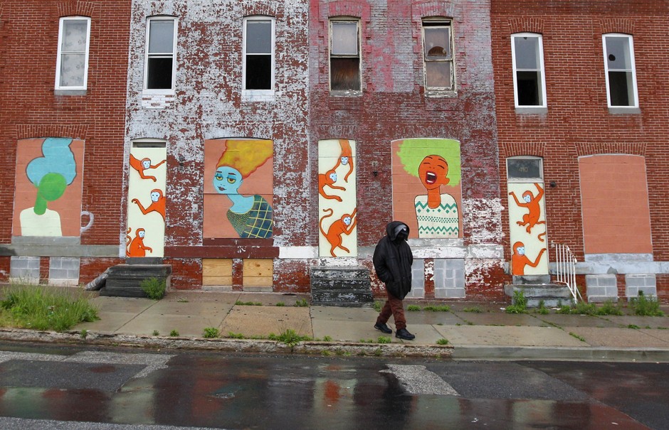 A man walks past a boarded-up row of houses as rain falls in Baltimore