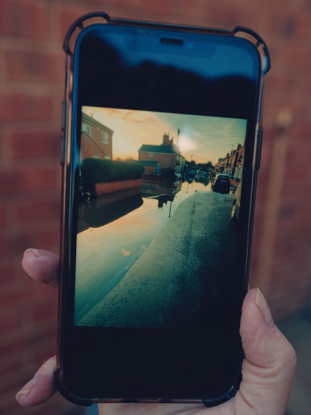 Paula Buchanan’s neighbor holds a phone showing a video of earlier flooding near their homes.