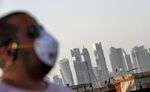A man wearing a mask walks past the Doha skyline in Qatar.