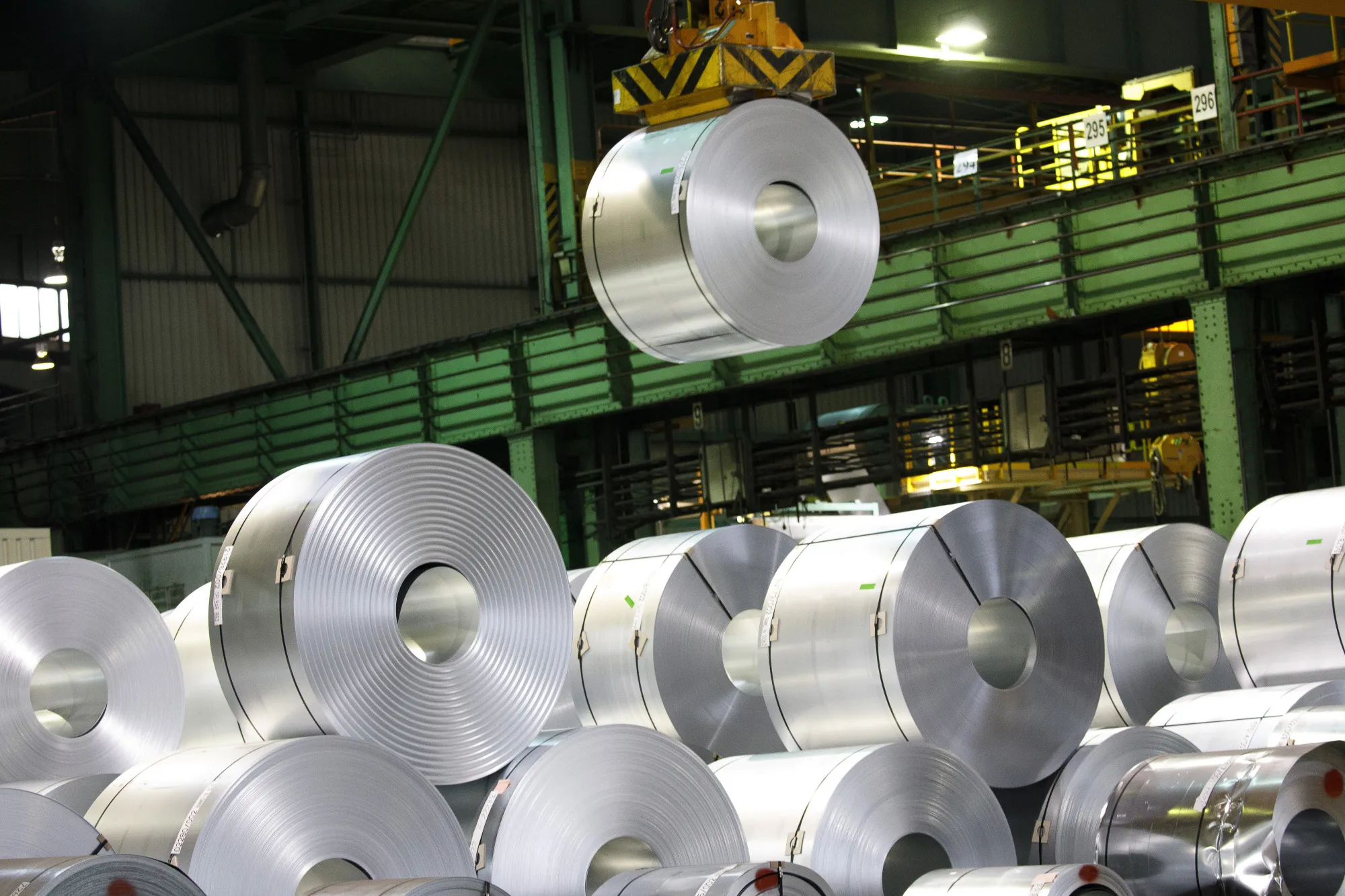 A crane maneuvers a roll of steel above a storage area ahead of shipping.&nbsp;