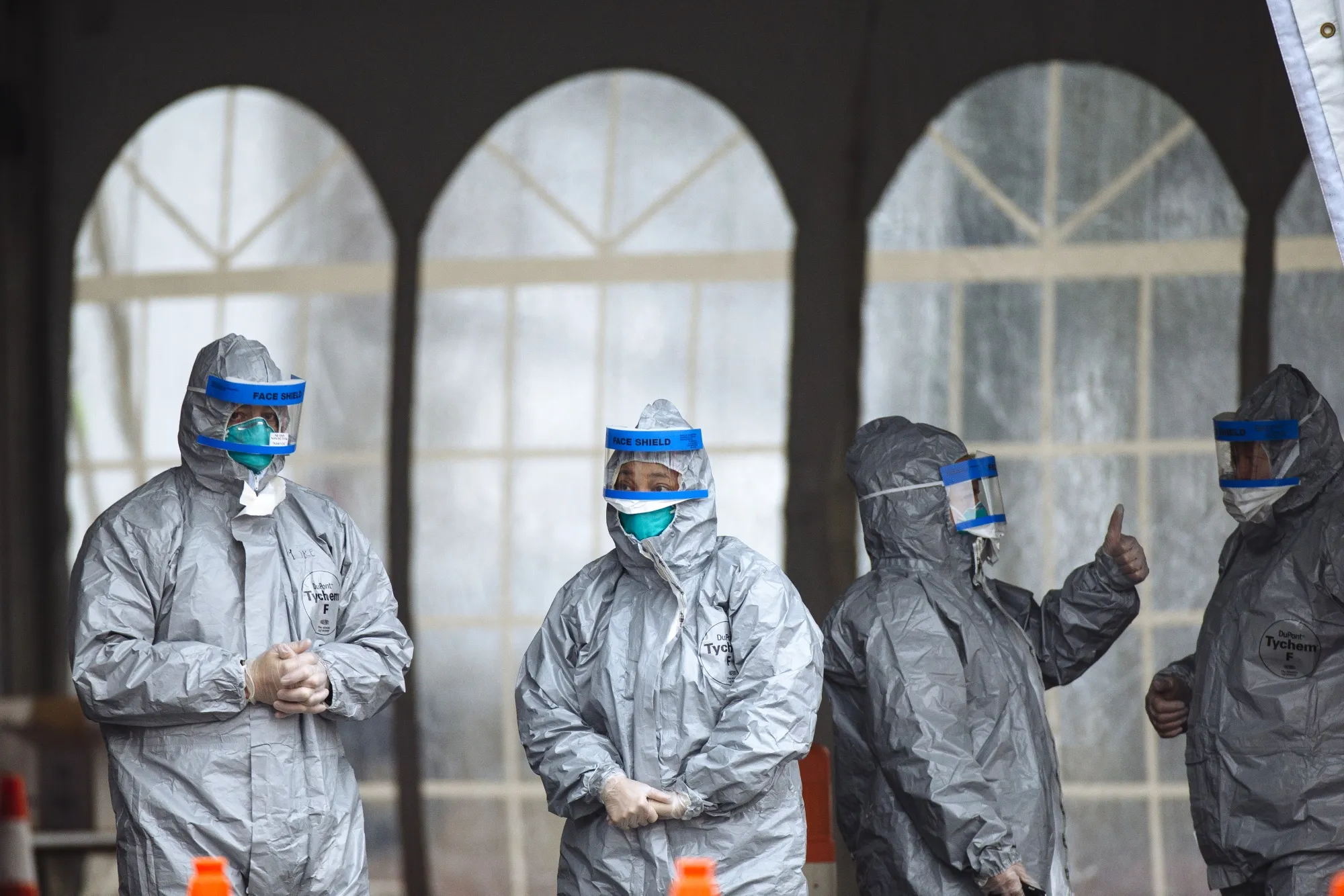 Health care workers in protective suits stand outside a COVID-19 drive-through testing facility at Glen Island Park in New Rochelle.