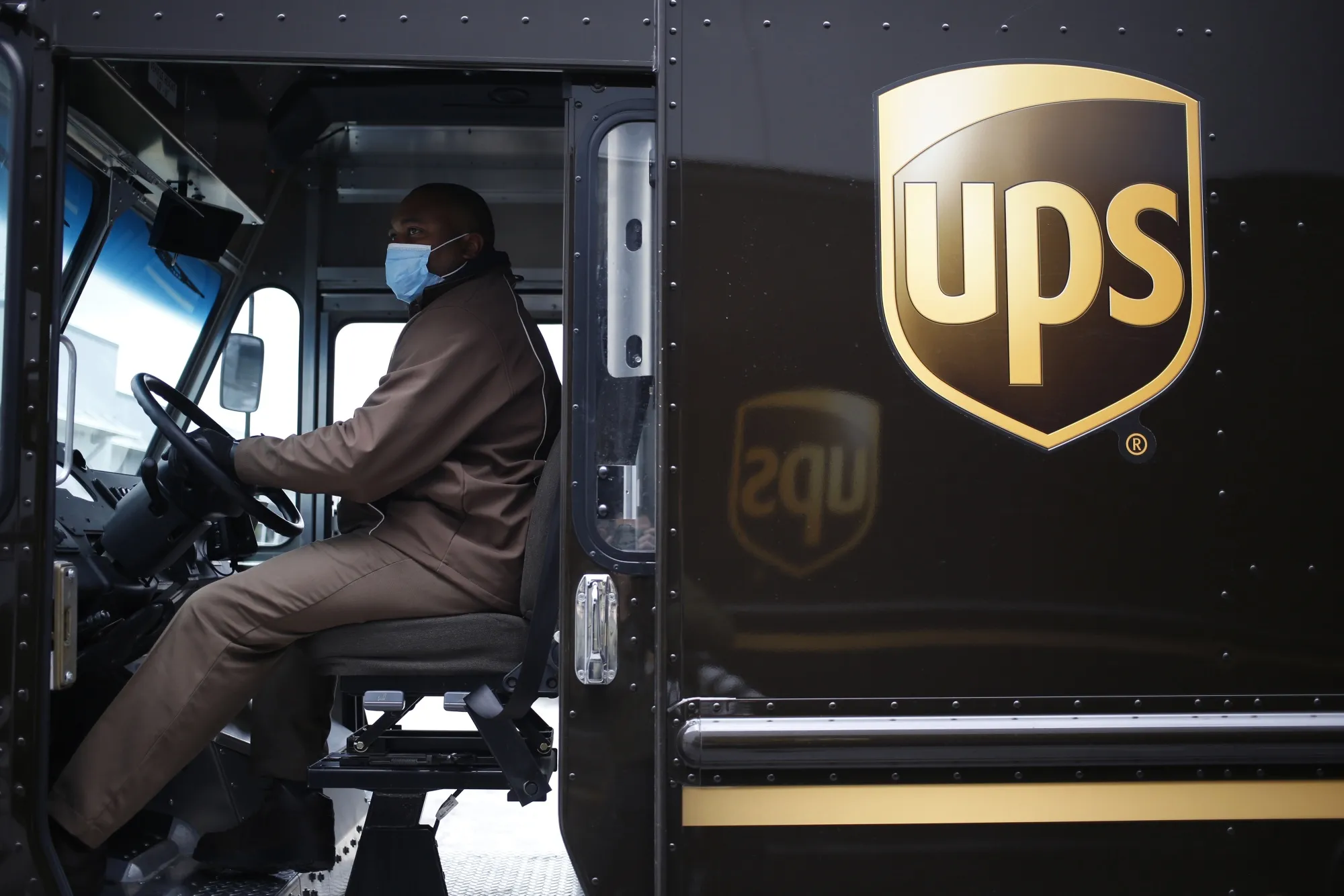 A UPS delivery driver wears a protective mask while driving a delivery truck in Louisville, Ky.