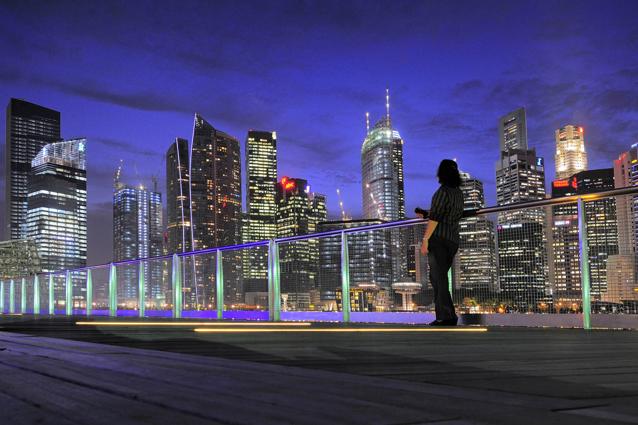 A woman on the waterfront boardwalk of the Marina Bay Sands shopping mall takes in the view across of the Singapore business district skyline, on Wednesday, October 13, 2010.
