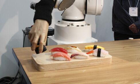 A visitor looks at a robot placing a set of waxwork sushi on a plate during a demonstration at the International Food Machinery and Technology Exhibition in Tokyo, on June 9, 2009.