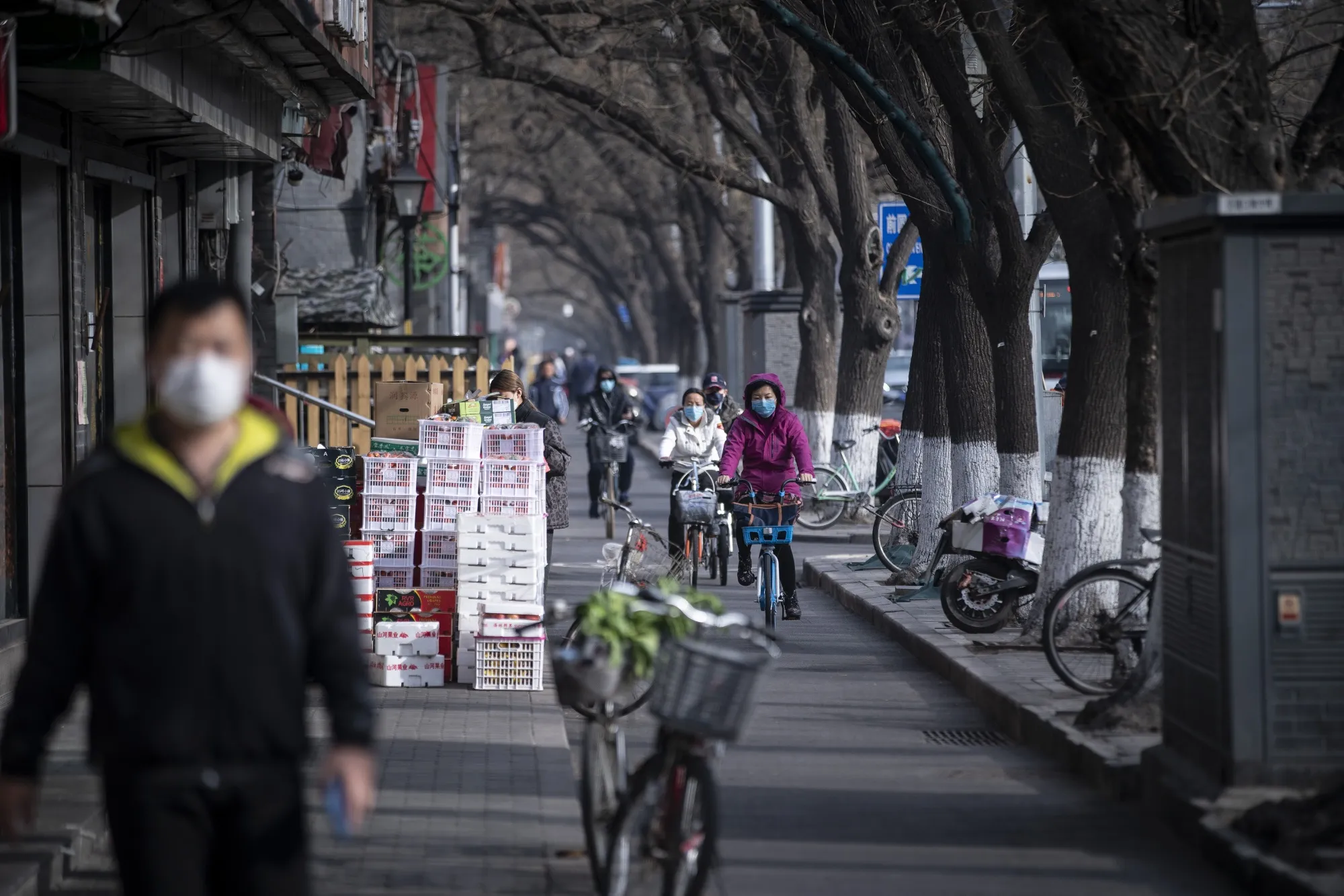 Commuters wearing protective masks ride bicycles down a street in Beijing on March 18.