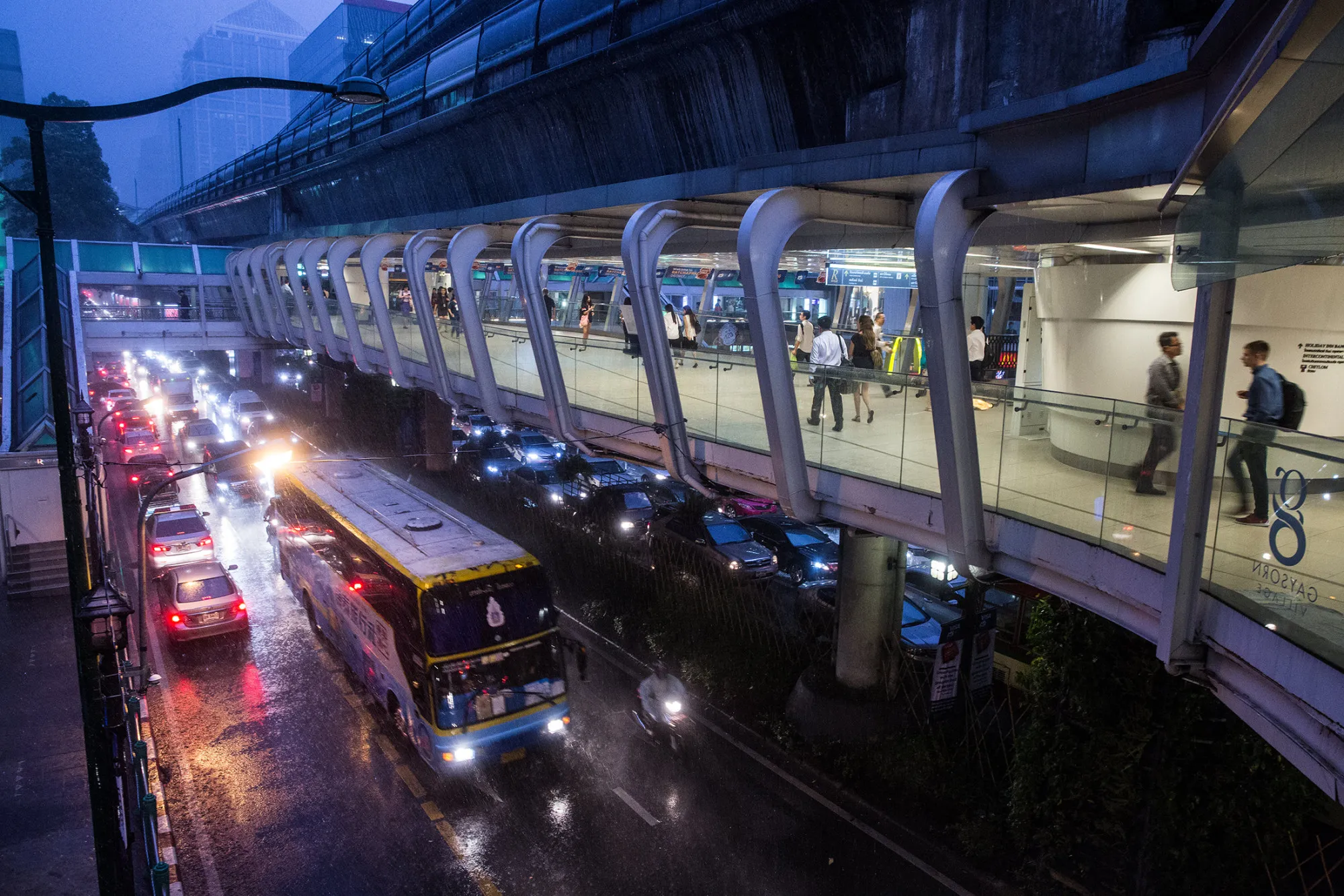 Pedestrians walk on a foot bridge above traffic as it rains at dusk in Bangkok, Thailand, on June 21, 2017.
