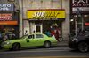 A taxi pulls out of a parking spot in front of a Subway in the Brooklyn.