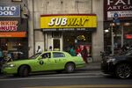 A taxi pulls out of a parking spot in front of a Subway in the Brooklyn.