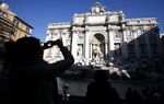 Tourists take photographs in front of the Trevi fountain in Rome, Italy.