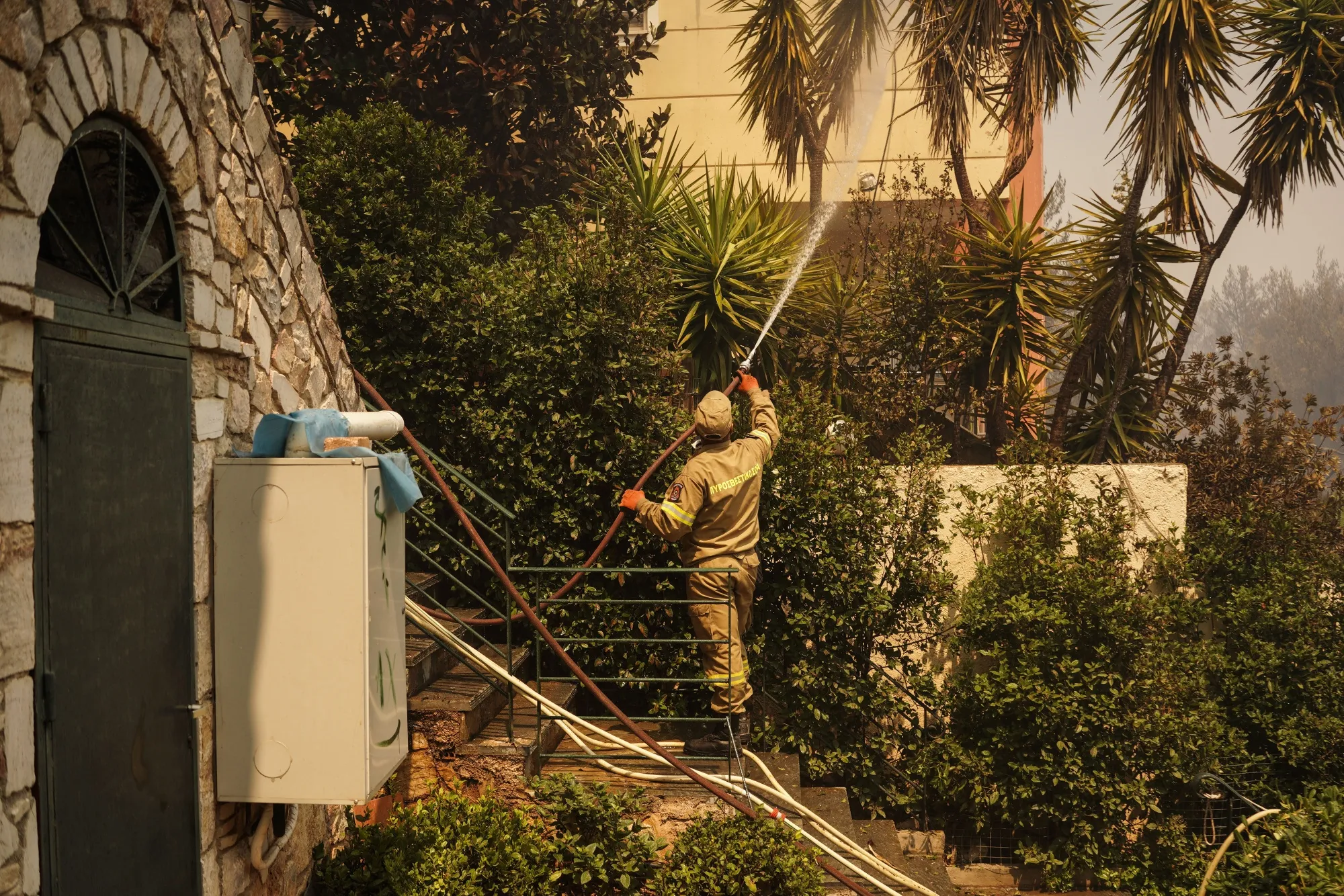 A firefighter douses foliage with water beside a residential property during a wildfire in Dioni, near Athens, on Aug. 12.