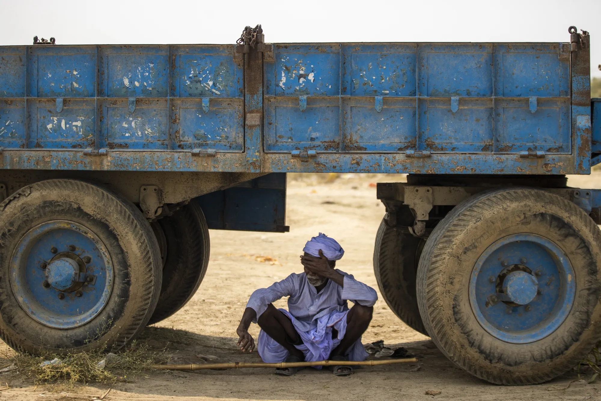 A man sits in the shade under a truck in Uttar Pradesh, India.