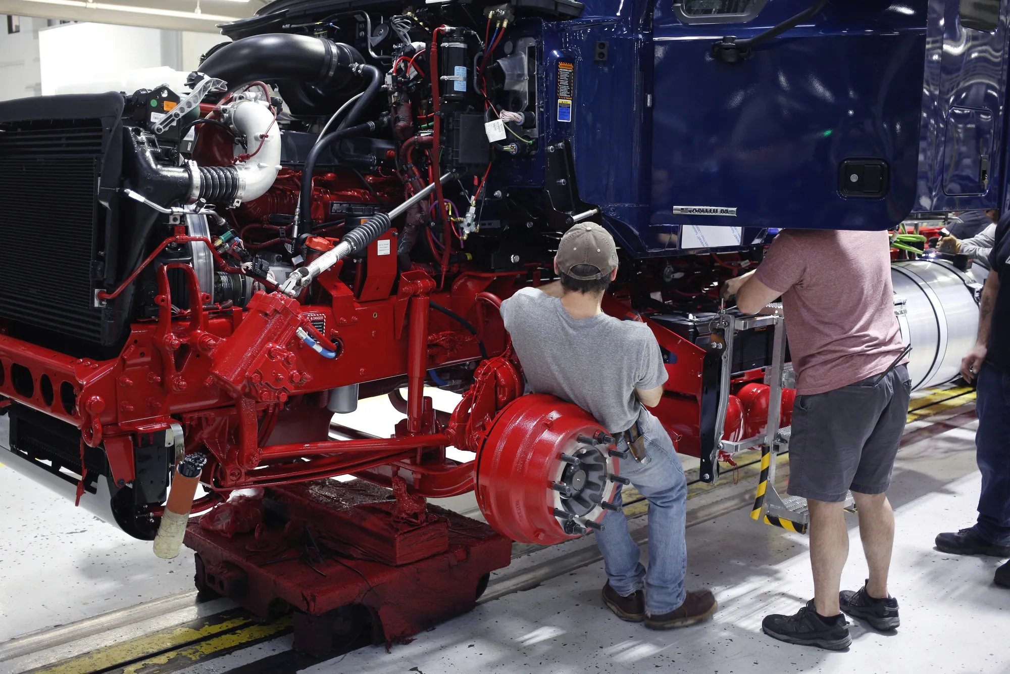 Workers install parts underneath a semi truck cab at an assembly facility in&nbsp;Pennsylvania.