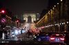 Vehicles sit at traffic lights as the Arc de Triomphe stands beyond at night in Paris.